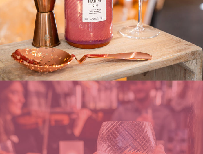 Harris Gin bottle with a cocktail and bar tools on a wooden surface, blurred background of people.
