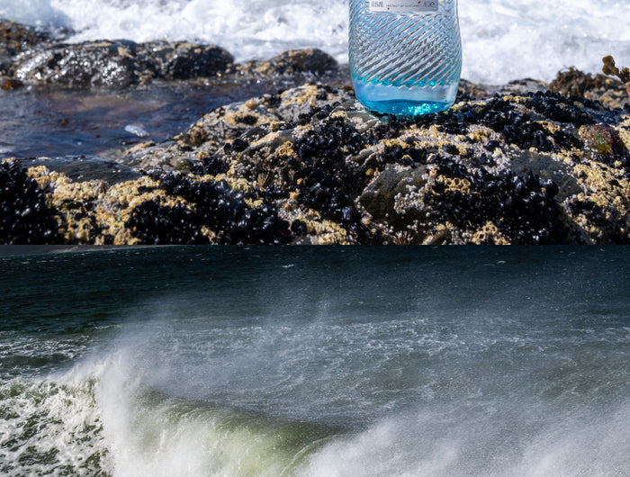 Bottle of Harris gin on a rocky shore with ocean waves in the background